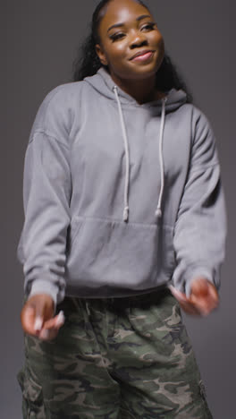 Vertical-Video-Studio-Portrait-Shot-Of-Young-Woman-Dancer-Wearing-Hoodie-Dancing-In-Against-Grey-Background-In-Slow-Motion-1